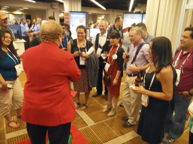 John Measner Magic Engaging a Crowd at a Corporate Tradeshow Corporate magician John Measner performing close-up magic for a laughing and engaged group of attendees on a tradeshow floor